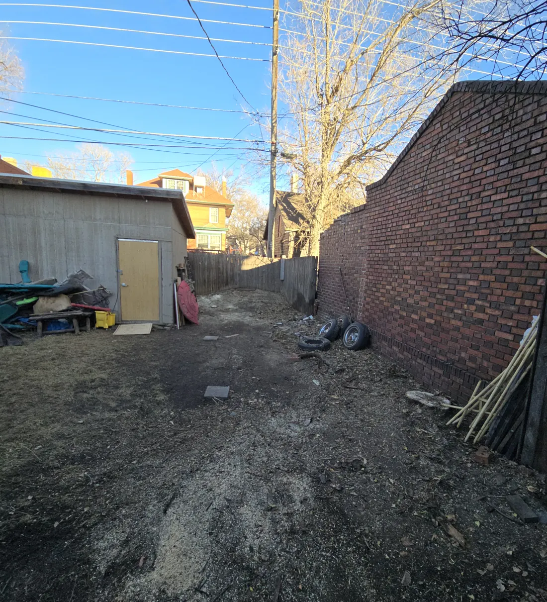 Narrow side yard between a shed and a brick wall, raked clean after a tree removal